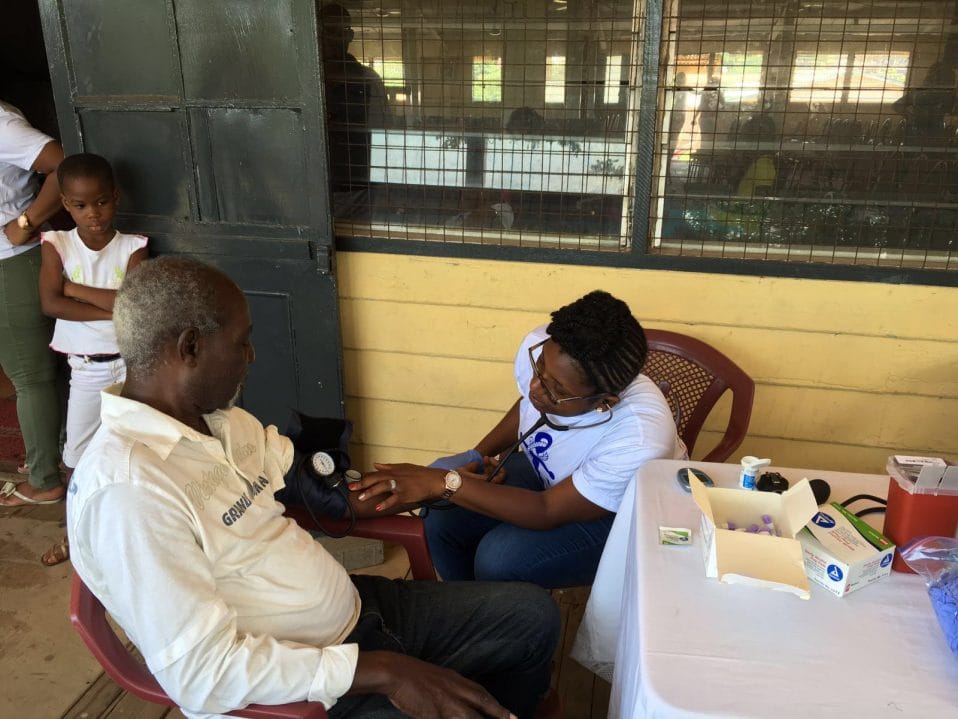 Community health worker conducting blood pressure screening in rural Ghana CHPS compound 2026